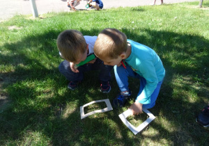 Dwóch chłopców ogląda przez lupę trawę na ogrodzie przedszkolnym.